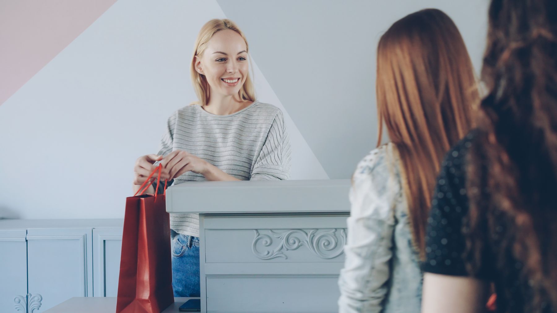 Dependienta sonriente entregando una bolsa roja a dos clientes en una tienda